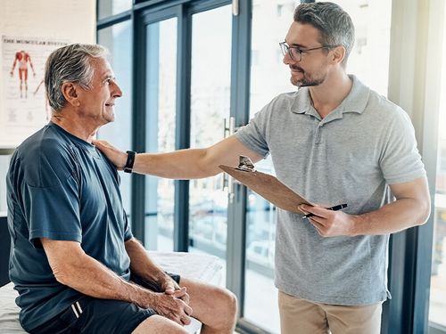 Physiotherapeut und Patient bei einem Gespräch. Beide schauen sich lächelnd an.