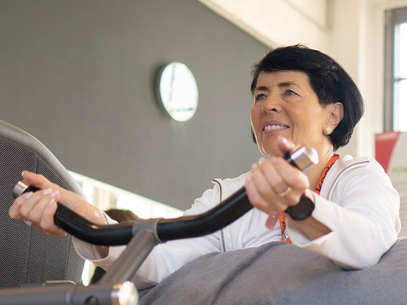 Patientin lächelnd an einem Kraftgerät für die Arme.