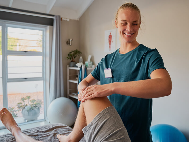 Physiotherapeutin ĂĽber bei einem erwachsenen Patienten eine Ăśbung am rechten Kniegelenk durch.