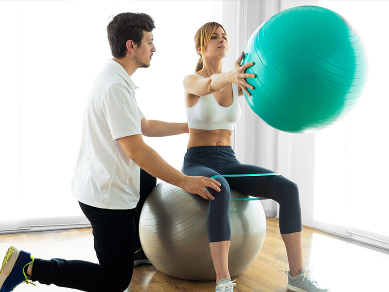 Physiotherapeut bei eienr Übung mit einer Patienten mit Gymnastikbällen.