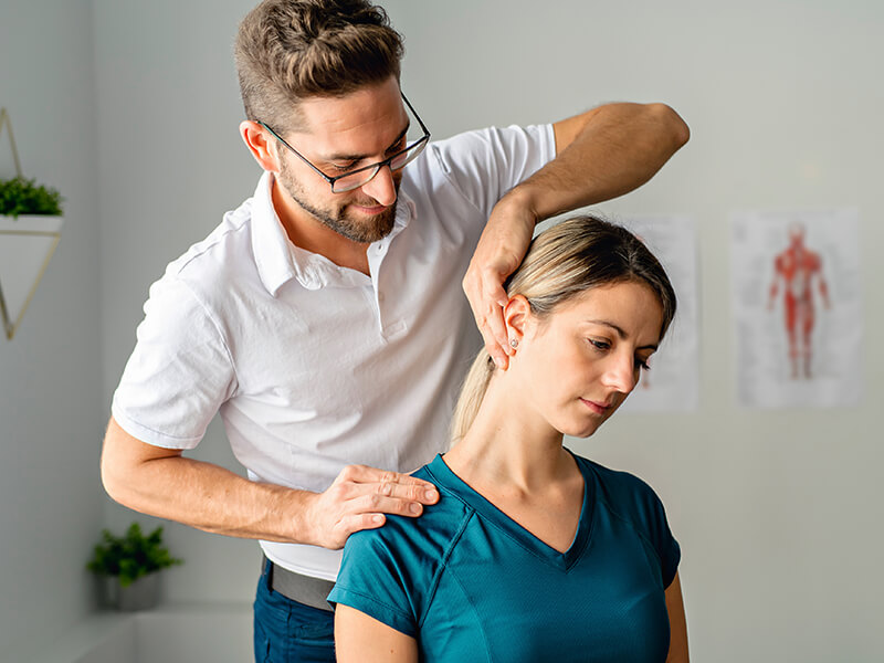Physiotherapeut fĂŒhrt bei einer erwachsenen Dame eine Ăbung an Schulter-und Nackenbereich durch.