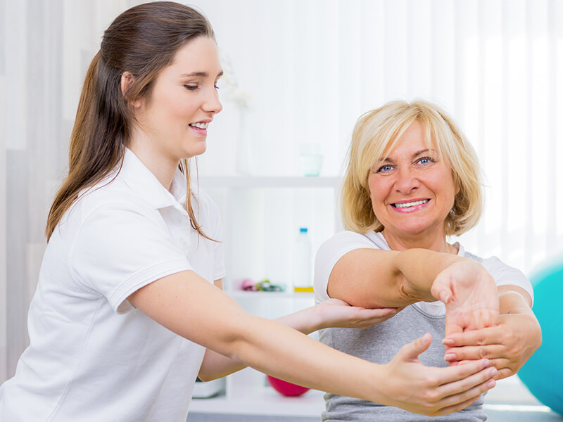 Physiotherapeutin und Patientin bei einer Ăśbung fĂĽr die Handgelenke.